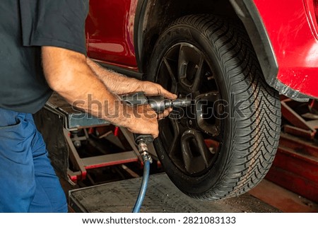 Professional auto mechanic using a pneumatic impact wrench to remove wheel bolts during tire replacement and wheel service in an automotive workshop