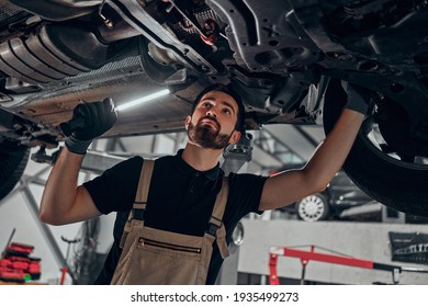 Professional auto mechanic working on the undercarriage of a car. Diligence, attention, inspection, examination, annual checkup, safety, insurance, professionalism, vehicle concept. Bottom view. - Powered by Shutterstock