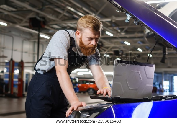 A\
professional automotive electrician diagnoses car errors using a\
laptop against the background of a service\
station