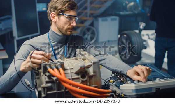 Professional Automotive Engineer in\
Glasses with a Computer and Inspection Tools is Testing an Used\
Electric Engine in a High Tech Laboratory with a Concept Car\
Chassis.