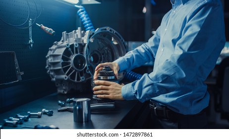Professional Automotive Engineer in Glasses is Working on Transmission Gears in a High Tech Innovative Laboratory with a Computer Screens.