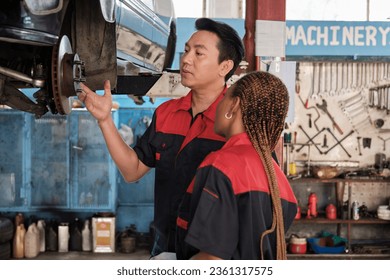 Professional automotive supervisors inspect and discuss car suspension repair work with female African American mechanic worker at service garage, and fix specialist occupations in the auto industry. - Powered by Shutterstock