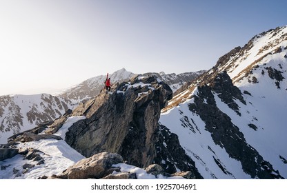 A professional backcountry skier with a backpack and skis stands on a rock in the mountains. Concept: Hike, Freedom, Explore, Journey. Enjoying idyllic view of mountain range.