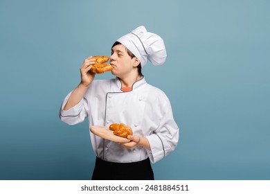 Professional baker smelling a croissant while holding a tray of pastries in studio setting isolated on blue background. Bakery concept - Powered by Shutterstock