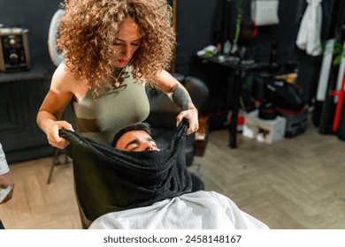 Professional barber applies a hot towel to a man's face in a modern barbershop, enhancing the beard grooming experience with a focus on relaxation and style. - Powered by Shutterstock