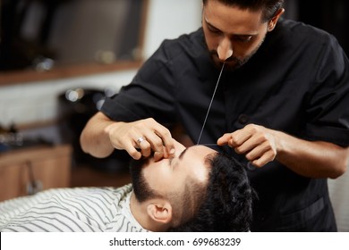 Professional barber doing eyebrow threading for male client in chair.  - Powered by Shutterstock