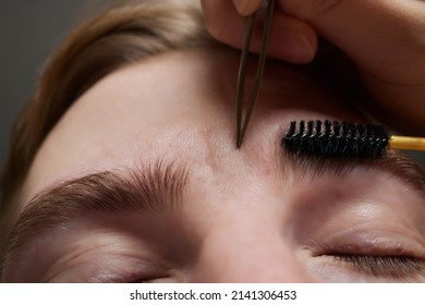 Professional barber doing threading procedure and correcting shape of eyebrows to young male client with tweezer in barber shop. Barber at work. Brow care concept. Plucking brows. - Powered by Shutterstock
