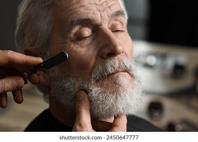 Professional barber shaving client's beard with blade in barbershop - Powered by Shutterstock