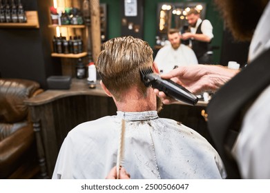 Professional barber using comb and electric shaver to cut side hair. Close-up view of male customer getting stylish haircut.