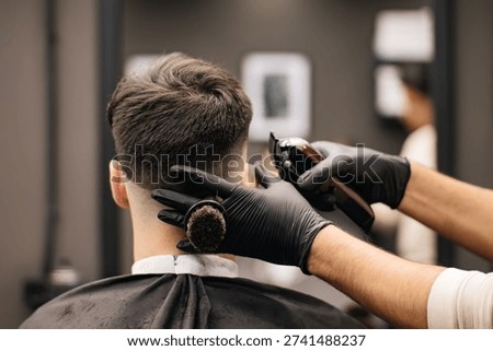 Professional barber using an electric trimmer and a neck brush to create a precise fade haircut. Close-up of a masculine hairstyling process in a modern barbershop.