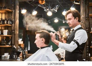 Professional barber using hairspray to finish hairstyle. Stylish hairdresser making final touches. Young customer getting fresh haircut. - Powered by Shutterstock