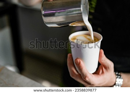 Professional barista hands pouring steamed milk into coffee paper cup making coffee.