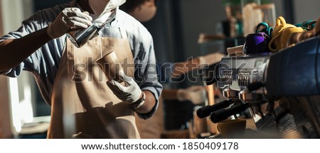 Professional barista makes cappuccino during social distance. African american male hipster in apron, protective gloves and mask, pours milk in takeaway paper cup for client, cropped, panorama