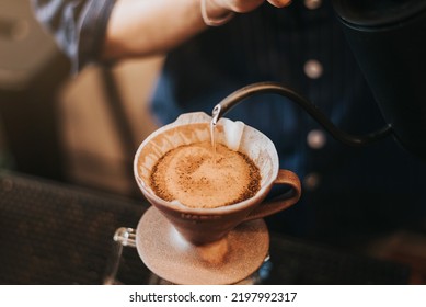 Professional barista making filtered drip coffee in coffee shop. Close up of hands barista brewing a drip hot espresso, pour over coffee with hot water and filter paper in cafe. - Powered by Shutterstock