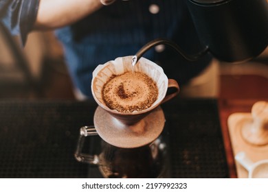 Professional barista making filtered drip coffee in coffee shop. Close up of hands barista brewing a drip hot espresso, pour over coffee with hot water and filter paper in cafe.