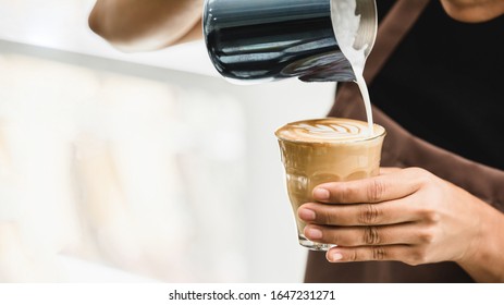 Professional barista pouring steamed milk into coffee glass cup making beautiful latte art Rosetta pattern in cafe - Powered by Shutterstock