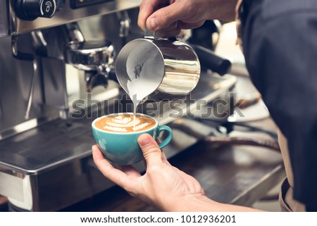 Professional barista pouring steamed milk into coffee cup making beautiful latte art Rosetta pattern