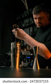Professional barman using beaker pours alcoholic drink into shaker with one hand and holds bottle in other