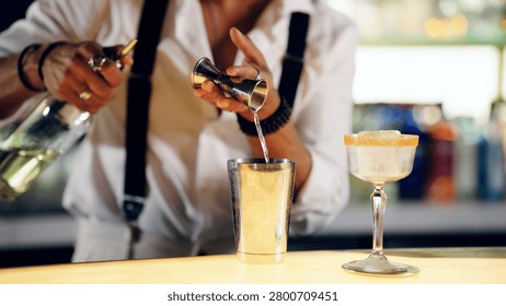 Professional bartender precisely pouring liquid with a jigger into a shaker, crafting a custom cocktail on a glowing bar counter