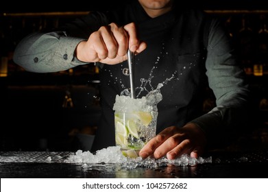Professional bartender prepare a fresh lime cocktail in the glass with an ice at the steel barstand
