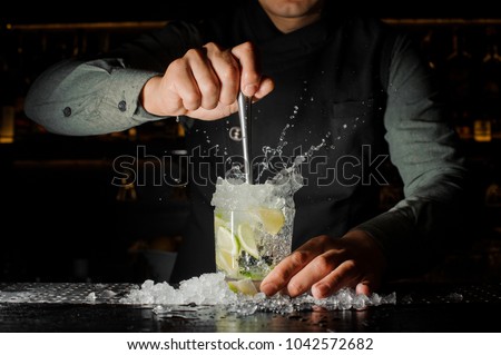 Professional bartender prepare a fresh lime cocktail in the glass with an ice at the steel barstand