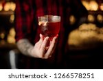 Professional bartender serving a glass of a Vieux Carre cocktail with big ice cube and orange zest on the steel bar counter on the blurred background