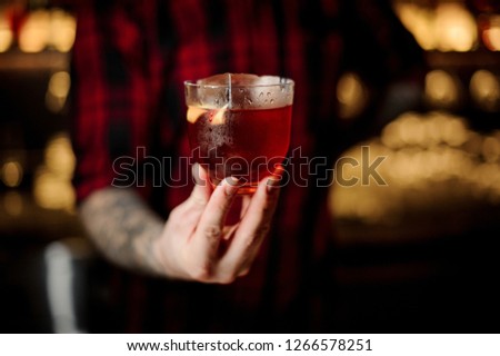 Professional bartender serving a glass of a Vieux Carre cocktail with big ice cube and orange zest on the steel bar counter on the blurred background [[stock_photo]] © 