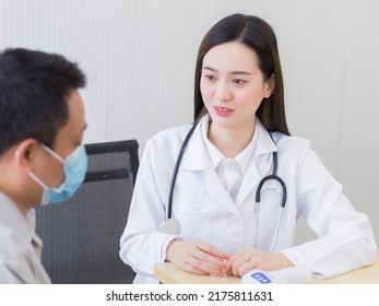 Professional Beautiful Young Asian Female Doctor Talking With A Man Patient About His Pain And Symptom While They Put On A Face Mask To Thermometer On Table At The Examination Room In Hospital.