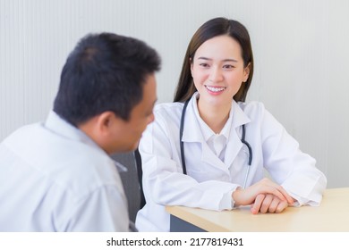 Professional Beautiful Young Asian Female Doctor Talking With A Man Patient About His Pain And Symptom While They Put On A Face Mask And Thermometer On Table At The Examination Room In Hospital.