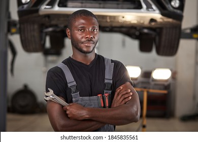 professional black auto mechanic looking at camera, handsome black guy in uniform is keen on repairing car. automobile in the background - Powered by Shutterstock