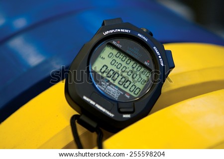 Professional black digital stopwatch and countdown timer with yellow and blue Olympic style rubber bumper plate weights for coaching, sports, personal trainer, interval training and workout routines