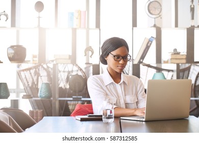 Professional Black Entrepreneur And Businesswoman Busy Working On Her Laptop Computer While Seated At The Head Of The Conference Table In The Business Lounge.