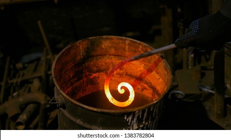 Professional blacksmith working with metal - quenching hot iron part of forged gate in water at forge, workshop. Handmade, craftsmanship and blacksmithing concept - Powered by Shutterstock