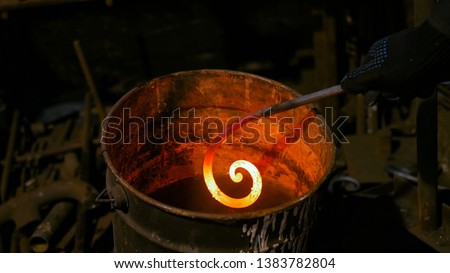 Professional blacksmith working with metal - quenching hot iron part of forged gate in water at forge, workshop. Handmade, craftsmanship and blacksmithing concept