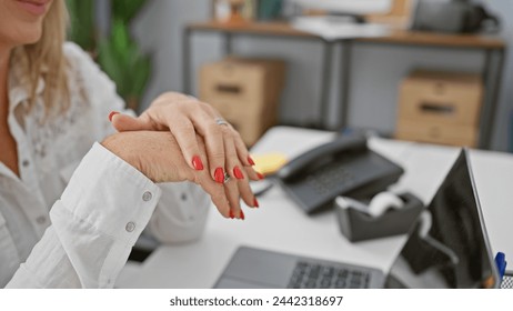 A professional blonde woman with red nails sits at her organized office workspace, surrounded by modern devices and stationery. - Powered by Shutterstock