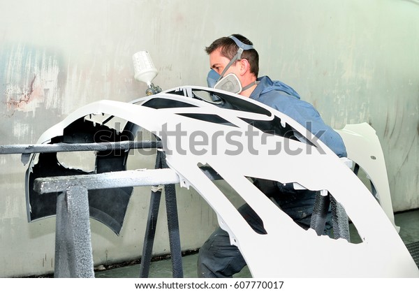 Professional\
body shop worker painting white car\
bumper.
