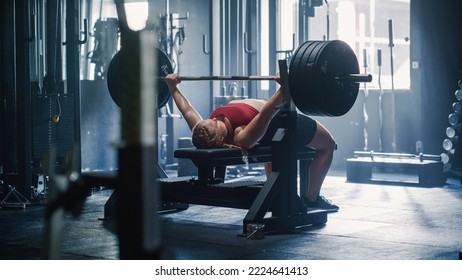 A Professional Bodybuilder Training by Lifting a Heavy Barbell In a Dark Gym. Female Energetic Athlete Doing Core Exercise with Bench Press Workout in an Empty Gym - Powered by Shutterstock