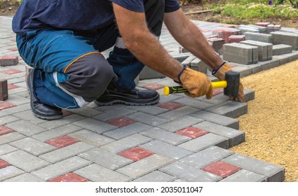 Professional bricklayers install new tiles or slabs for the roadway, sidewalks or patio on a foundation of lined sand. Laying gray concrete paving slabs in the courtyard of the house. - Shutterstock ID 2035011047