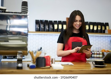 Professional brunette woman barista checking application notification on touchpad standing at bar in coffee shop, positive female manager of cafeteria using modern digital tablet for checking incomes - Powered by Shutterstock