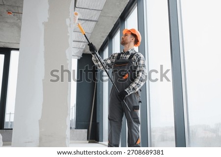Professional builder applying a paint roller while decorating the interior of a newly constructed apartment, showcasing skill and precision