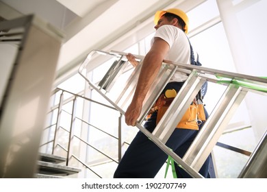 Professional builder carrying metal ladder up stairs  low angle view