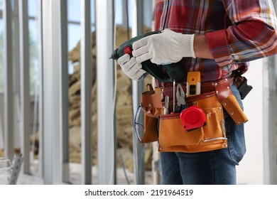 Professional Builder With Tool Belt And Power Drill Indoors, Closeup