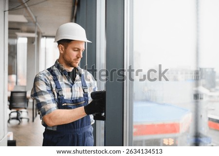 Professional builder using cordless screwdriver, installing window frames in a new office building, ensuring precise and secure placement
