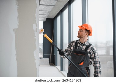 Professional builder using a paint roller, applying a fresh coat of paint to the walls of a building under renovation, demonstrating the process of interior finishing