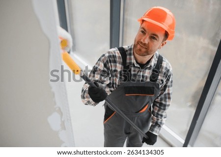 Professional builder using a paint roller, applying a fresh coat of paint to the walls of a building under renovation, demonstrating the process of interior finishing
