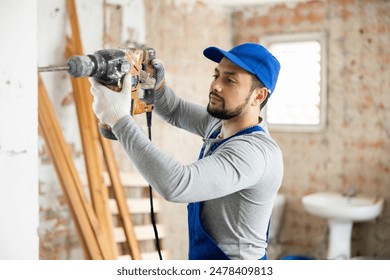 Professional builder working on a construction site during the capital repairs of a house drills a wall with a hammer drill