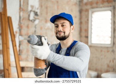 Professional builder working on a construction site during the capital repairs of a house drills a wall with a hammer drill