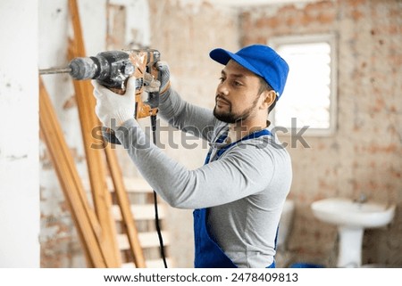 Professional builder working on a construction site during the capital repairs of a house drills a wall with a hammer drill