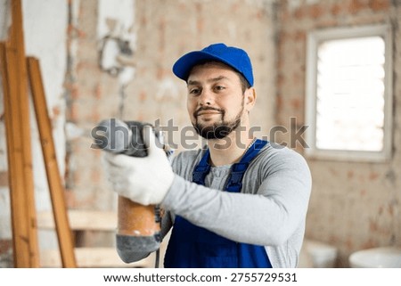 Professional builder working on a construction site during the capital repairs of a house drills a wall with a hammer drill