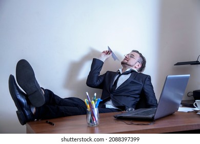 Professional burnout, laziness, unwillingness to work. Slacker businessman sitting in office with legs on the table and playing with paper plane. Horizontal image.